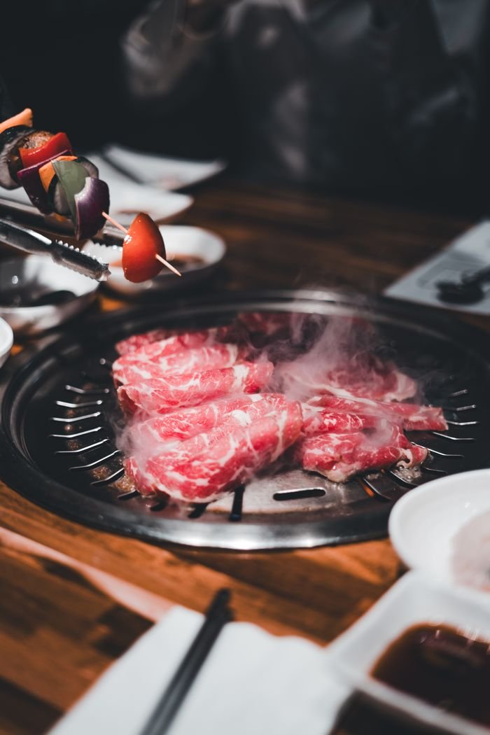 Appetizing grilled meat steaming on an indoor BBQ at a restaurant, with various sides on the table.